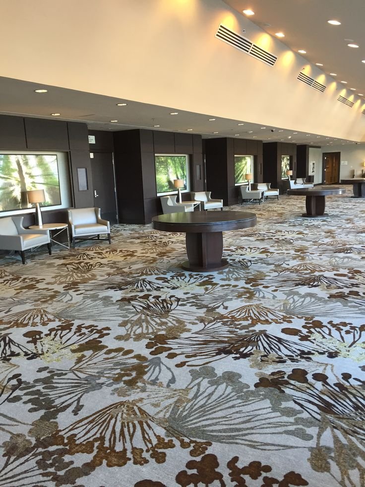 Brown and gold botanical print wall to wall carpet in hotel lounge with round tables
